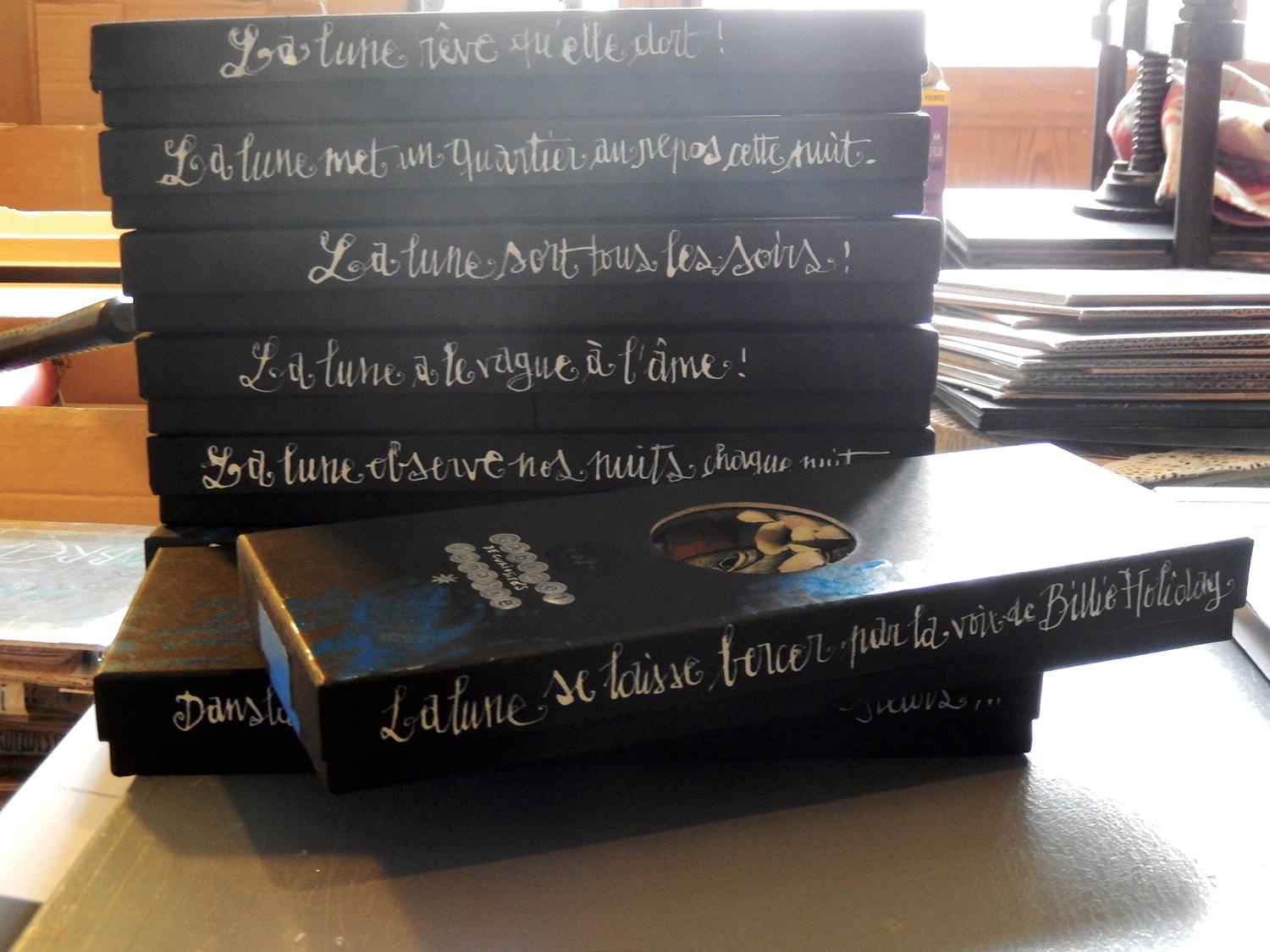 S É R I E “ C A B I N E T -D E C U R I O S I T É S- L U N A I R E ”. Série de 15 boîtes avec fenêtres en verre renfermant des lunes réalisées en carte à gratter. Dimensions des boîtes : L10,5 cm x H 27,5 cm x P 3,5 cm - Les tranches des boîtes